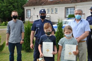 na pierwszym planie dwójka dzieci z nagrodami, a za nimi Dyrektor Szkoły Podstawowej w Sobiechach, obok Komendant Powiatowy Policji w Węgorzewie , a następnie wójt gminy Budry