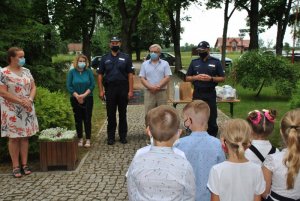 na pierwszym planie dzieci ze Szkoły Podstawowej w Więckach, a naprzeciwko nich od lewej dyrektorka Szkoły Podstawowej w Więckach, przewodnicząca Gminnej Komisji Rozwiązywania Problemów Alkoholowych w Budrach, Komendant Powiatowy Policji w Węgorzewie, Wójt gminy Budry oraz dzielnicowy