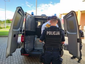 na pierwszym planie policjant stojący tyłem na drugim zatrzymany i policyjny radiowóz