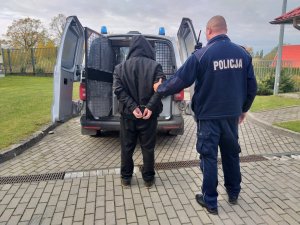 W tle radiowóz policyjny , zaś na pierwszym planie zatrzymany 53-latek razem z policjantem