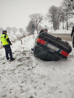 z lewej strony policjant, zaś z prawe samochód na dachu