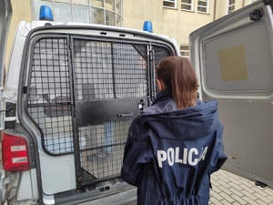 policjantka a przed nią radiowóz z zatrzymany w środku