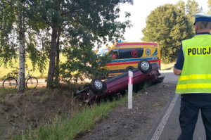 karetka pogotowia w tle samochód oraz na pierwszym planie policjant