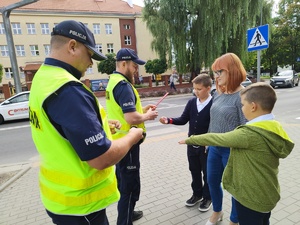 w tle policjanci z uczestnikami ruchu drogowego w trakcie działań Bezpieczna droga do szkoły