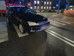 czarny samochód stoi na przejściu dla pieszych za nim stoi wóz strażacki